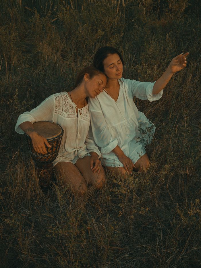 Two women in white outfits meditating outdoors with closed eyes, creating a serene and calming scene.
