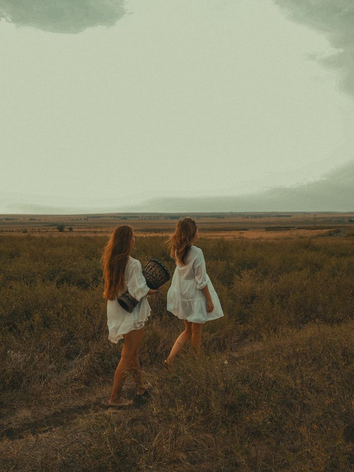 Two women in white dresses walking in a field with boho style at dusk, capturing travel and freedom.